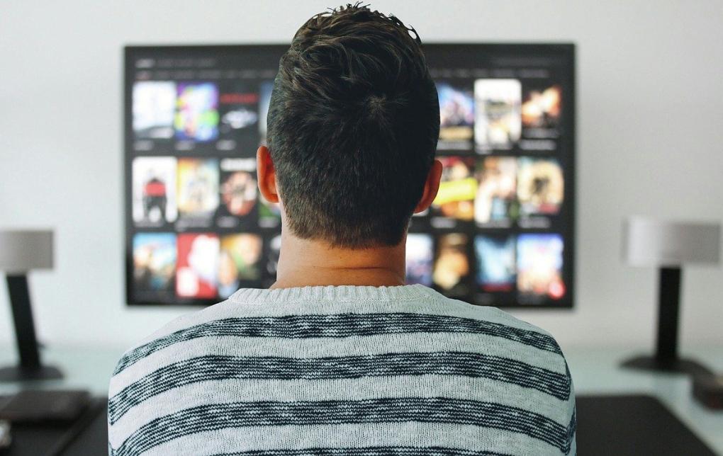 Foto: junger Mann von hinten stehend vor einem Fernsehrbildschirm