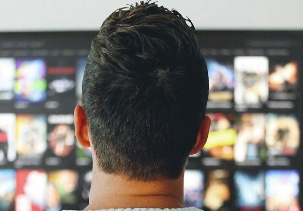 Foto: junger Mann von hinten stehend vor einem Fernsehrbildschirm