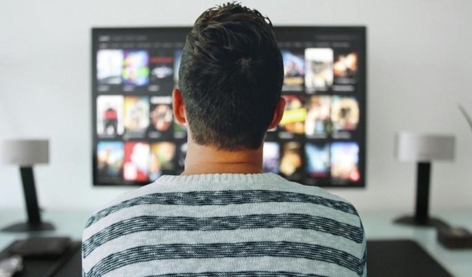 Foto: junger Mann von hinten stehend vor einem Fernsehrbildschirm