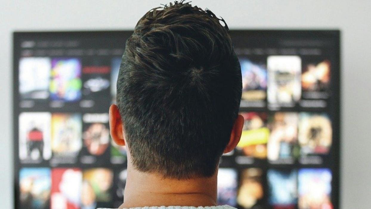 Foto: junger Mann von hinten stehend vor einem Fernsehrbildschirm