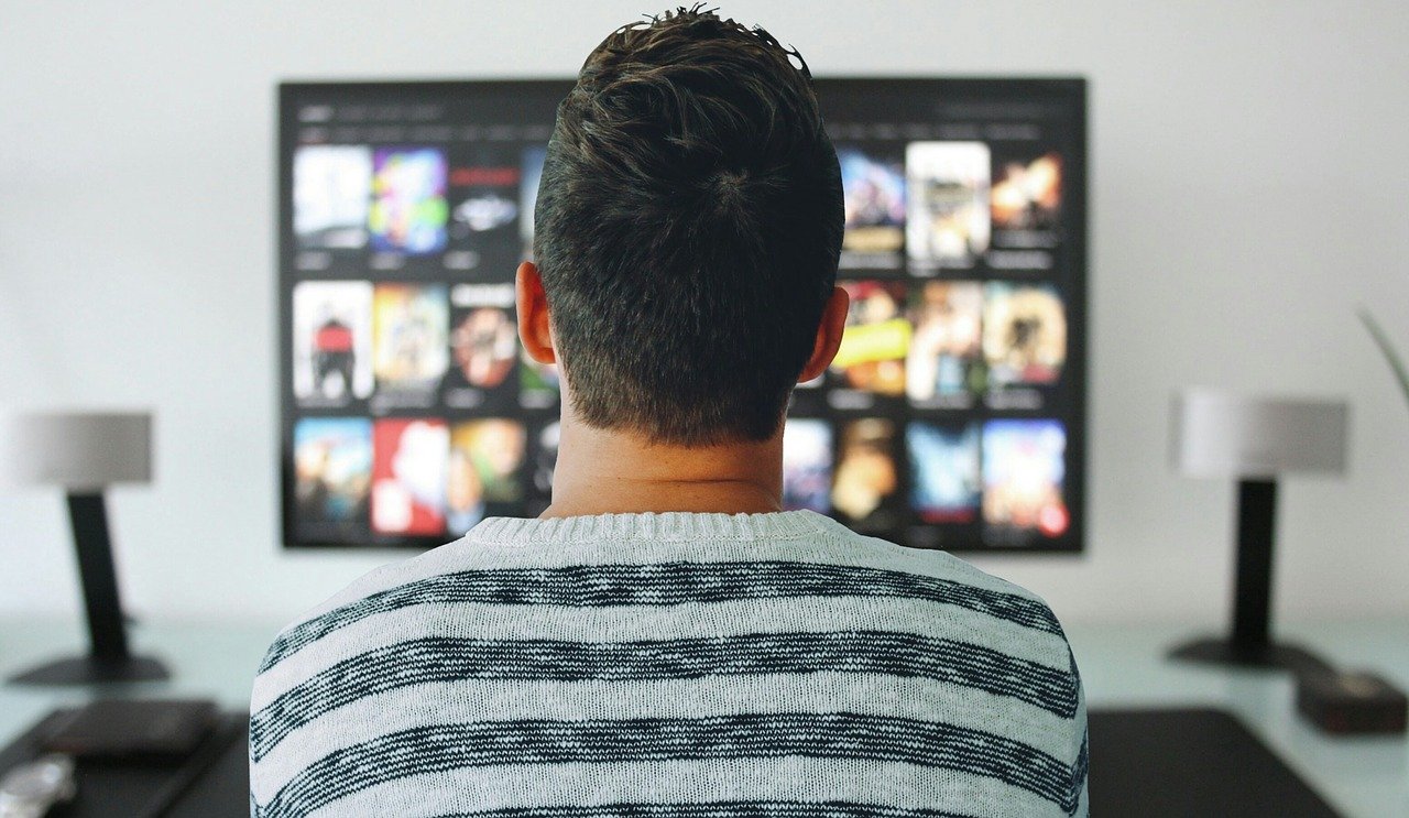 Foto: junger Mann von hinten stehend vor einem Fernsehrbildschirm