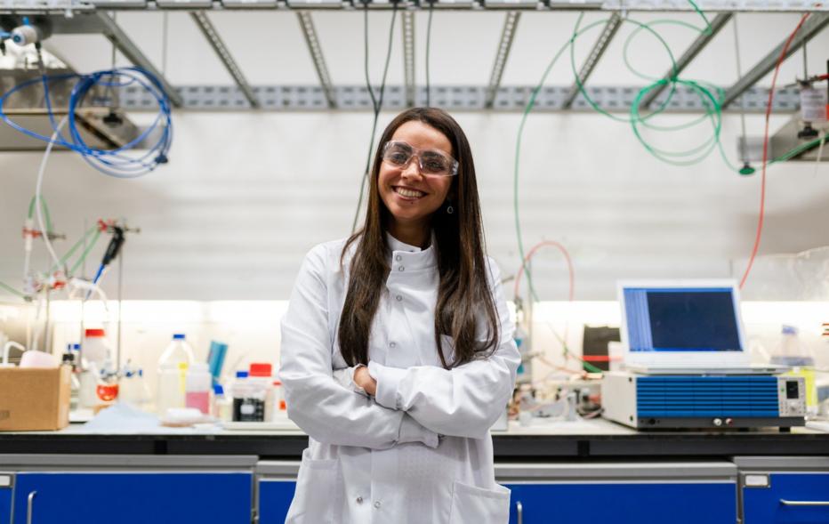 Foto: Frau mit weißem Kittel und Schutzbrille im Labor