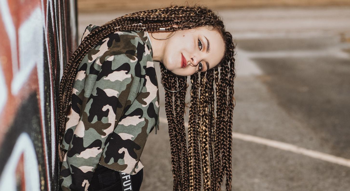 Foto: Jugendliche mit Braids Frisur angelehnt an eine Hauswand