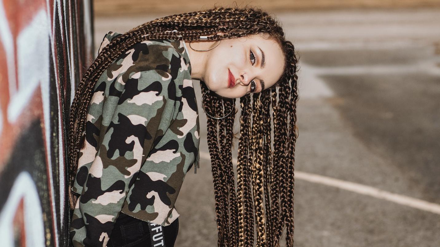 Foto: Jugendliche mit Braids Frisur angelehnt an eine Hauswand