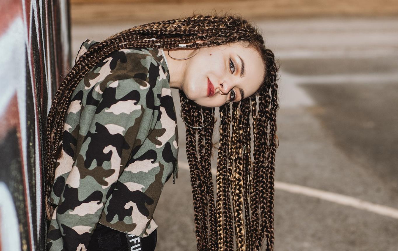 Foto: Jugendliche mit Braids Frisur angelehnt an eine Hauswand