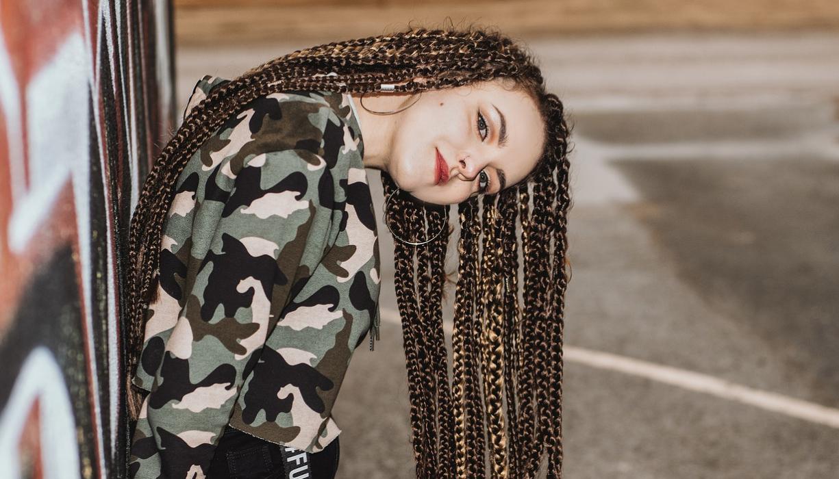 Foto: Jugendliche mit Braids Frisur angelehnt an eine Hauswand