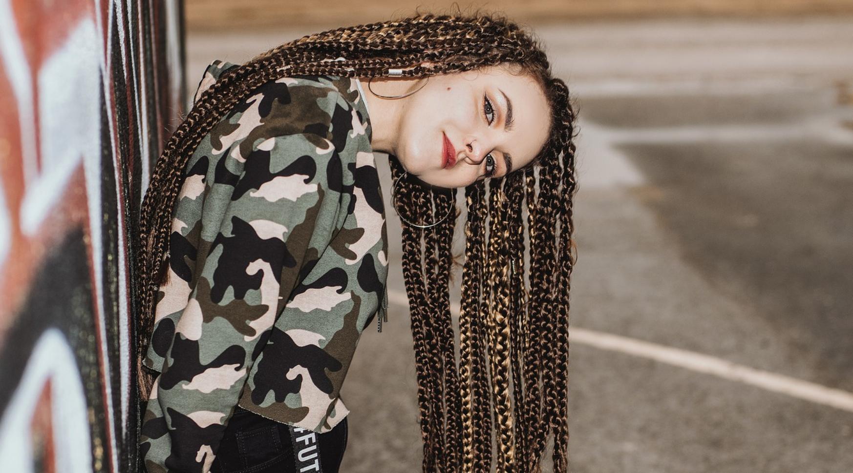 Foto: Jugendliche mit Braids Frisur angelehnt an eine Hauswand