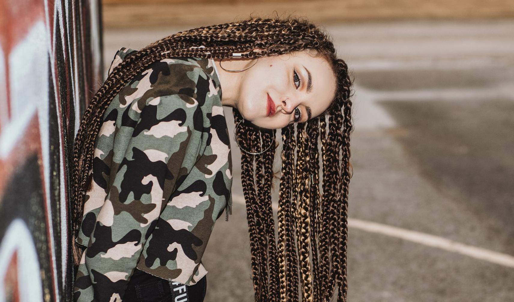 Foto: Jugendliche mit Braids Frisur angelehnt an eine Hauswand